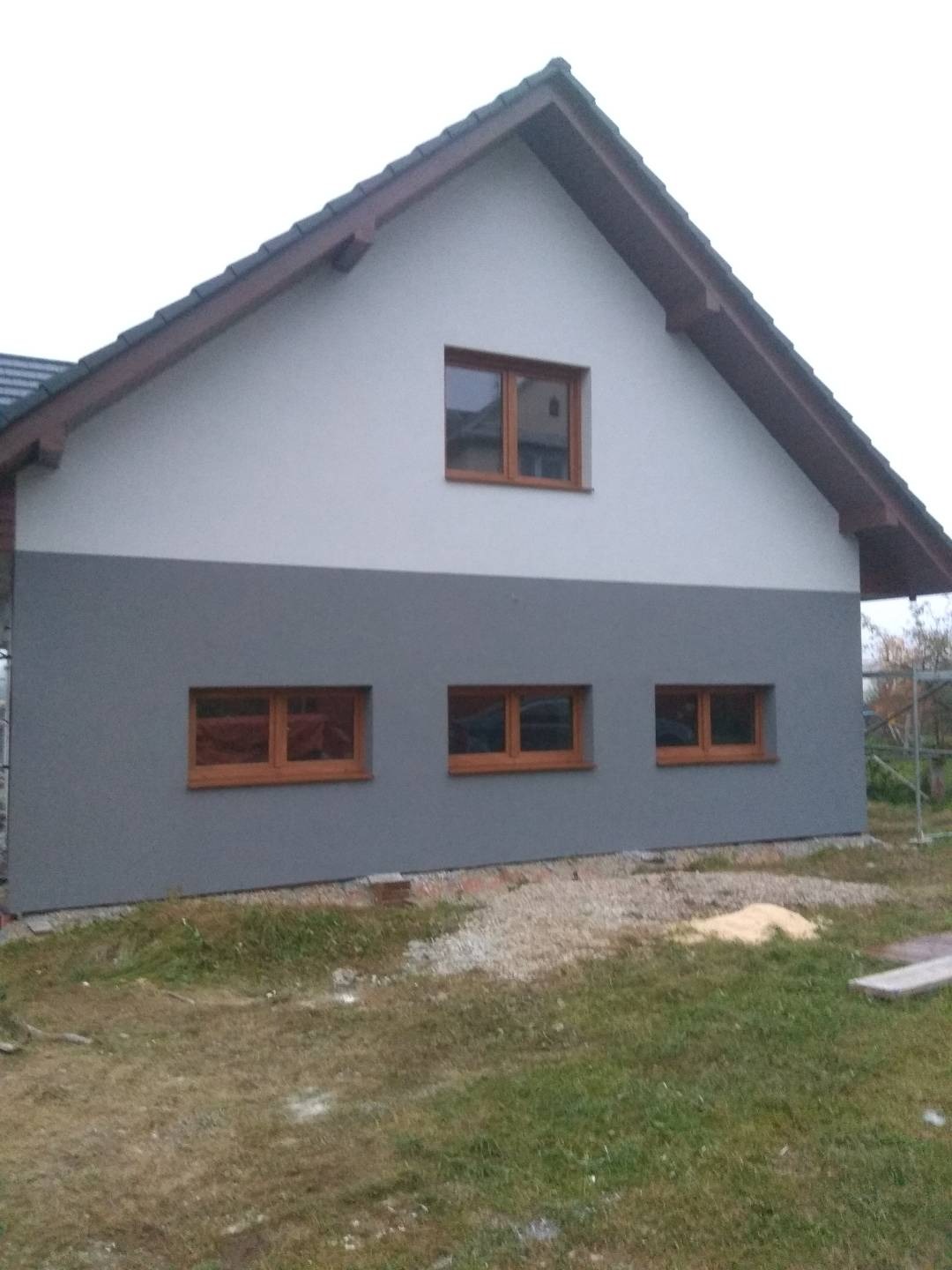 Dwukolorowa elewacja domu jednorodzinnego z trzema oknami na dole i jednym na górze, widoczne ślady po pracach budowlanych.