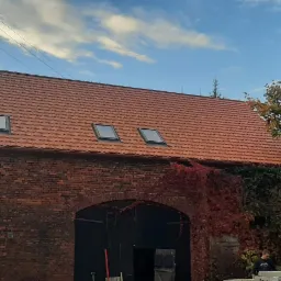 Czerwona dachówka z oknami dachowymi na budynku z czerwonej cegły we Wschowie, częściowo porośniętym bluszczem.