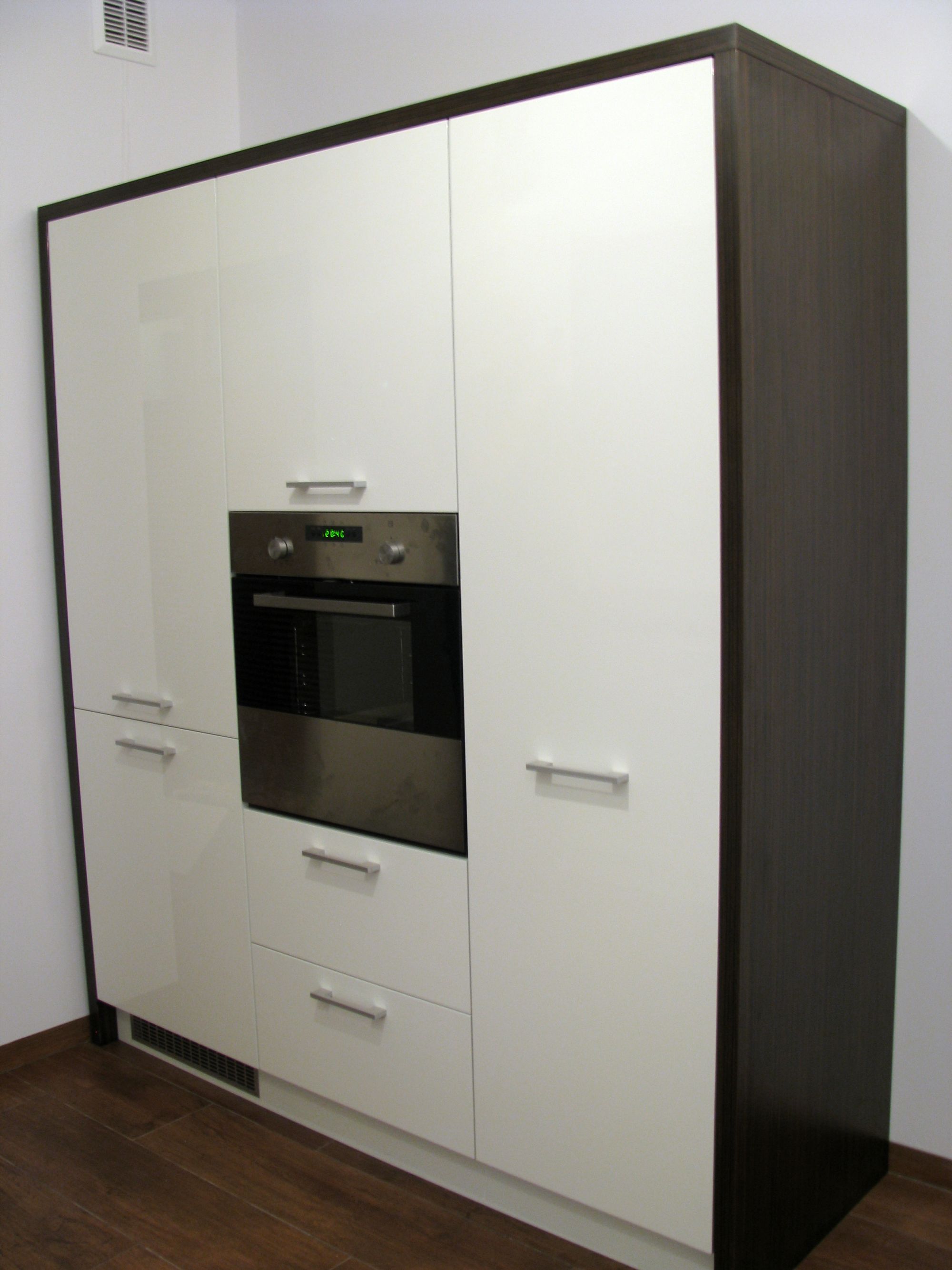 Wysoka zabudowa kuchenna z białymi, lakierowanymi frontami i ciemnobrązowymi bokami, z piekarnikiem w zabudowie, zrealizowana w Częstochowie.