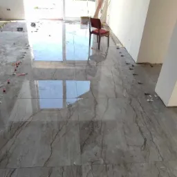 Układanie płytek podłogowych imitujących marmur w jasnym pomieszczeniu, widoczne plastikowe krzyżyki dystansowe i poziomica laserowa.