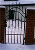 Kuta brama ogrodzeniowa z czarnego metalu, osadzona między dwoma ceglanymi słupkami, pokryta warstwą śniegu.