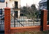Metalowe ogrodzenie z ceglanymi słupkami i podmurówką, widok z zewnątrz posesji.