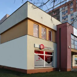 Budynek biurowy z logo 'proagents' oferujący ubezpieczenia, kredyty, leasing i pożyczki, z widocznymi plakatami salonu fryzjerskiego Venus w oknach na piętrze i stojakiem na rowery przed wejściem