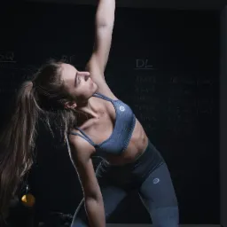 Kobieta w sportowym stroju wykonuje ćwiczenie z pomarańczowym kettlebellem w siłowni w Katowicach, na tle tablicy z zapisanymi wynikami ciężarów.