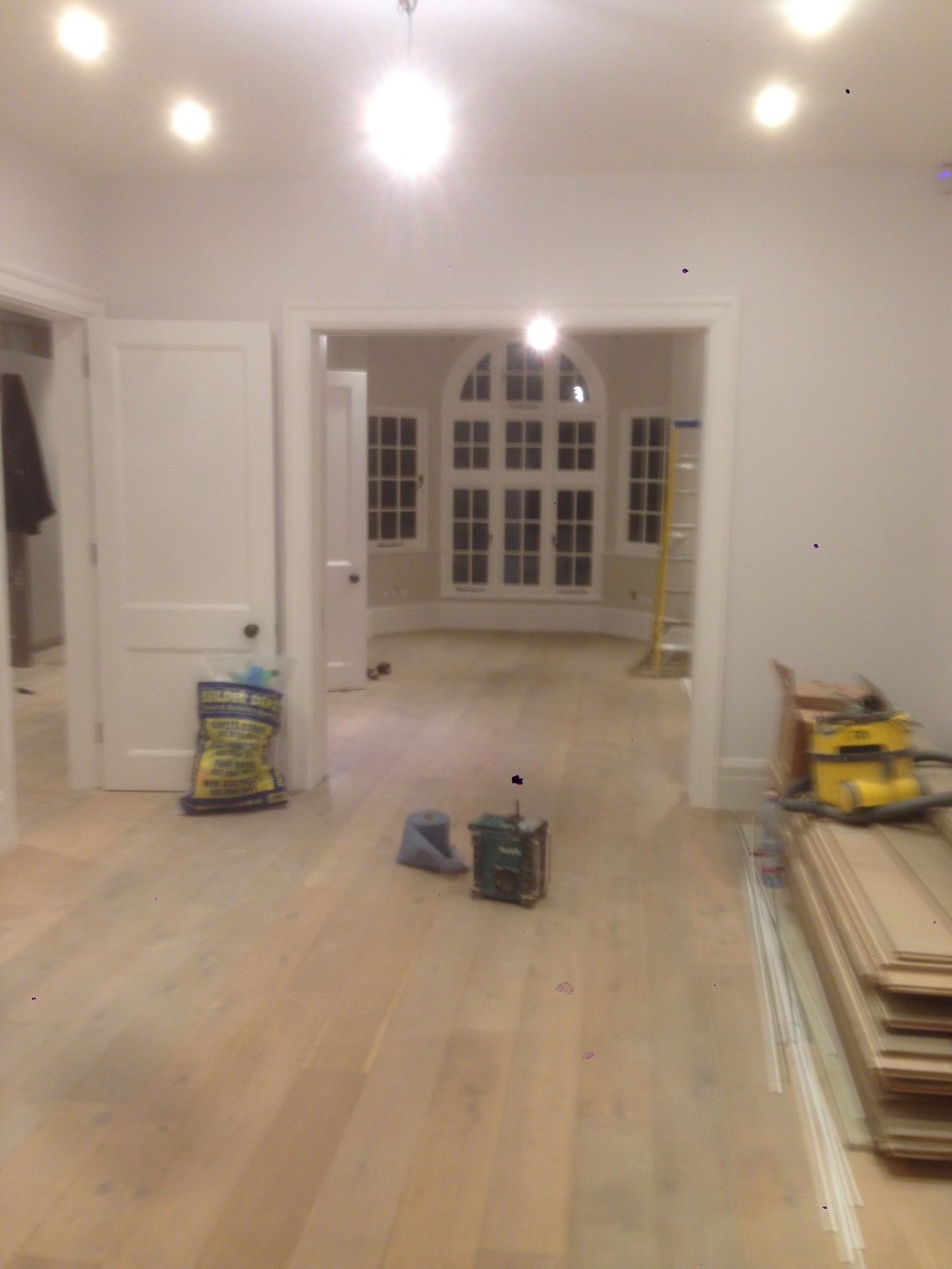 Jasna, odnowiona podłoga w pokoju z widokiem na okno z wieloma szybami, widoczny sprzęt do cyklinowania i materiały budowlane.