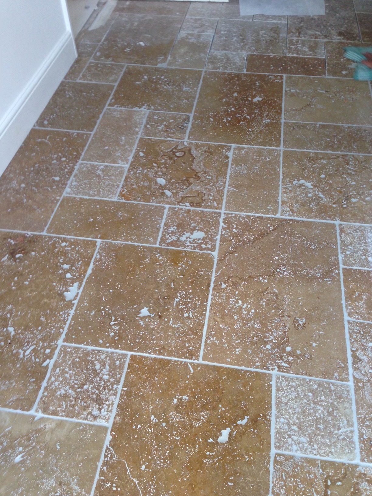 Ułożona podłoga z płytek trawertynowych w odcieniach beżu i brązu, z fugami w kolorze białym, na powierzchni widoczne pozostałości po fugowaniu.