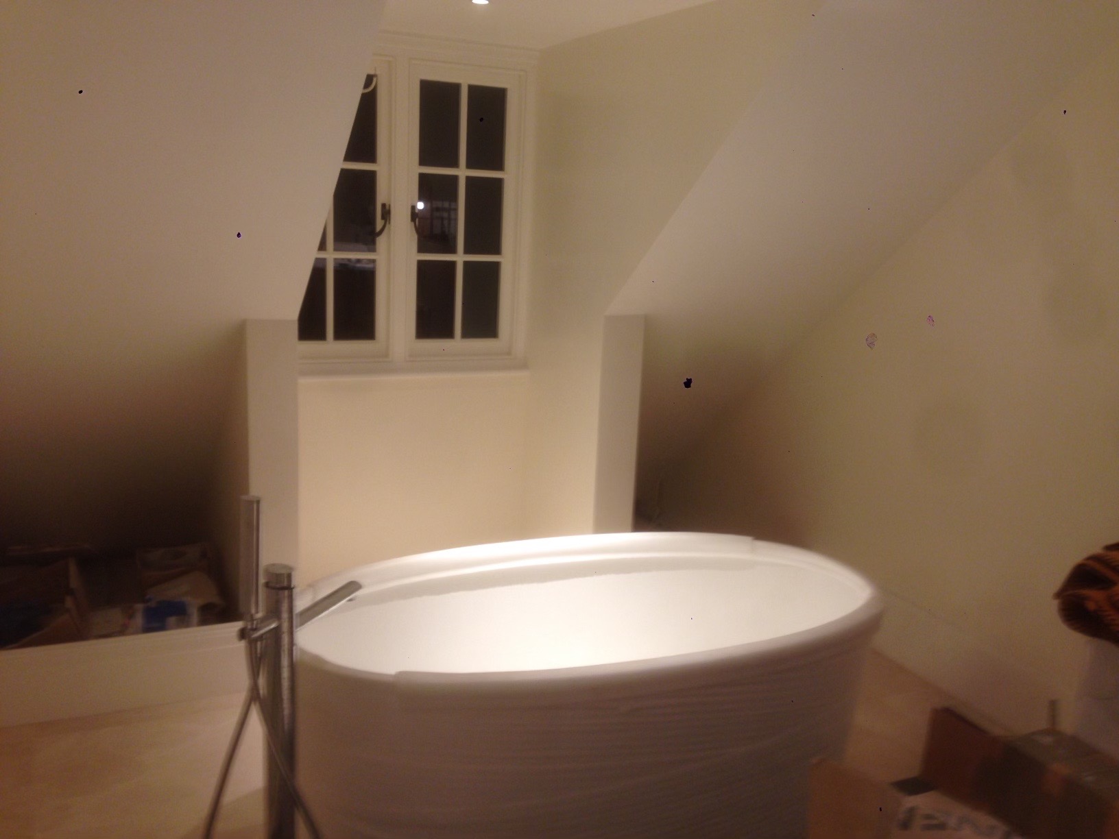 Nowoczesna, owalna wanna wolnostojąca w jasnej łazience na poddaszu, z widocznym oknem i metalową baterią.