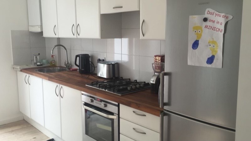 Wyposażona kuchnia z białymi szafkami, drewnianym blatem, płytą gazową, piekarnikiem i lodówką z rysunkiem dziecka przypiętym na magnes