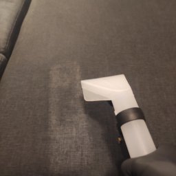 CzystoVit - Dysza odkurzacza piorącego na szarej kanapie, widoczny efekt czyszczenia, ręka w czarnej rękawicy.