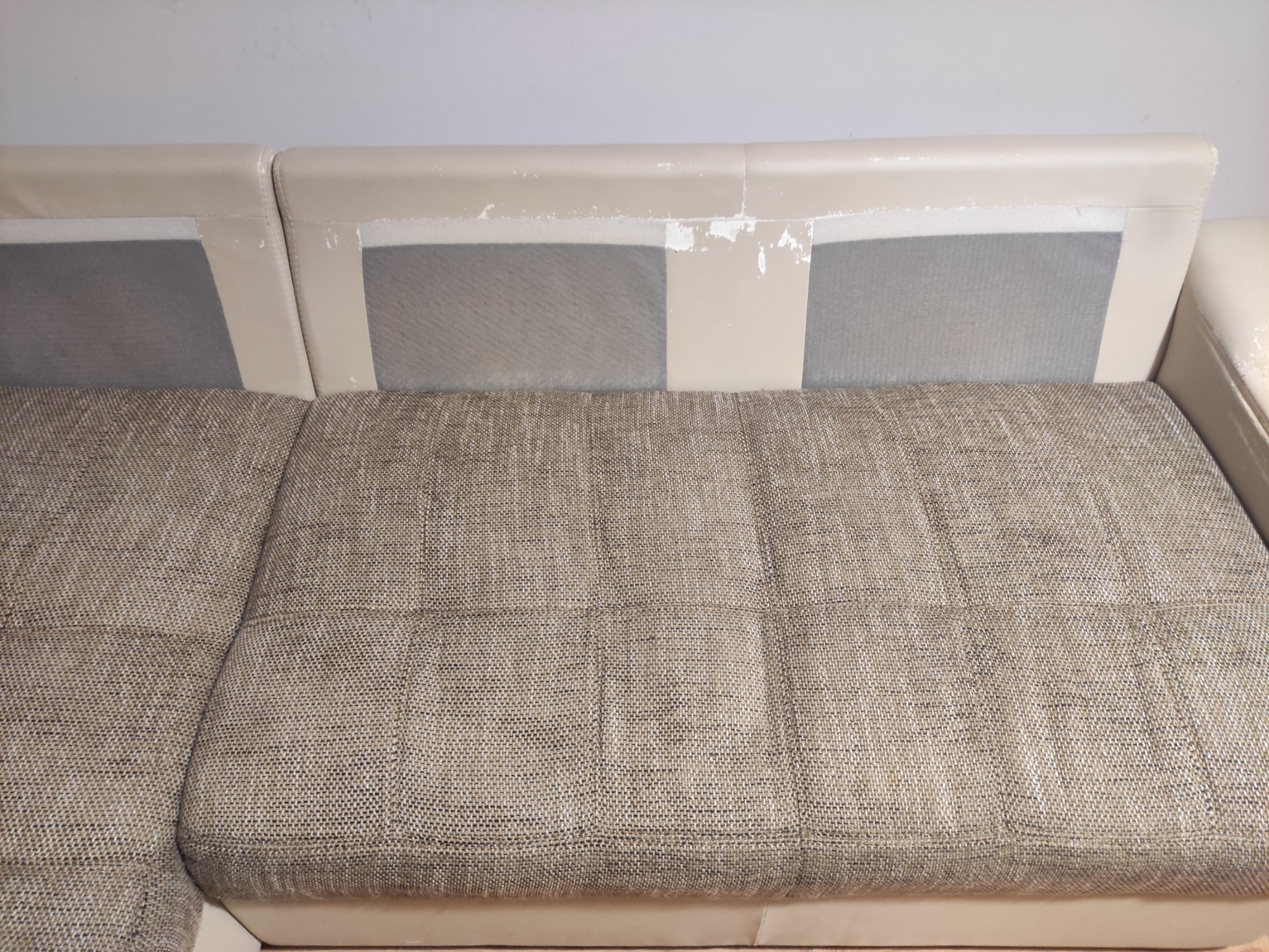Fragment narożnika z beżową tapicerką o wyraźnej fakturze, widoczne uszkodzenia na górnej krawędzi oparcia.