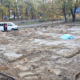 BudArtMagic Mykhailo Zagorodnyi - Przygotowanie terenu pod fundamenty domu: wykopane rowy, drewniane szalunki, biały bus z otwartymi drzwiami w tle, stos niebieskiego styropianu.