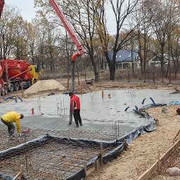 BudArtMagic Mykhailo Zagorodnyi - Wylewka fundamentów pod dom jednorodzinny w jesiennej scenerii, widoczna betoniarka z pompą, zbrojenie i pracownicy budowlani.