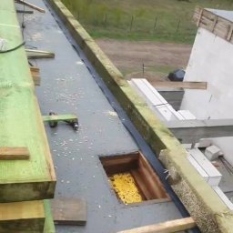 BudArtMagic Mykhailo Zagorodnyi - Widok z góry na budowę domu z betonu komórkowego w Pruszkowie, widoczny fragment dachu z otworem i żółtą izolacją oraz przygotowane drewniane elementy konstrukcyjne.