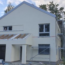 BudArtMagic Mykhailo Zagorodnyi - Nowo wybudowany dom jednorodzinny z garażem w stanie surowym zamkniętym, otynkowany na jasnożółto, z widocznymi rusztowaniami i elementami drewnianej konstrukcji dachu.