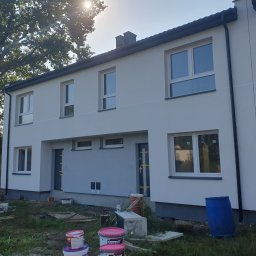 BudArtMagic Mykhailo Zagorodnyi - Bliźniak w trakcie prac wykończeniowych elewacji, widoczne puszki z farbą i niebieska beczka, na tle drzew i błękitnego nieba.