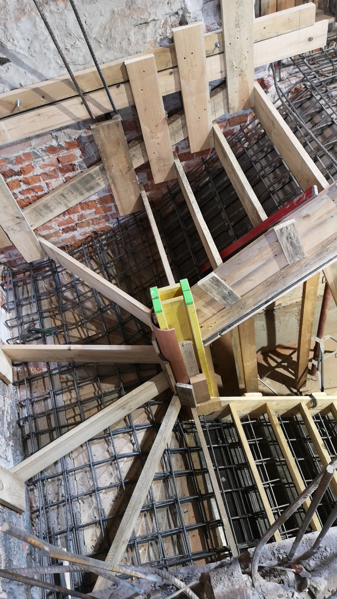 Zbrojenie fundamentów pod schody z drewnianym szalunkiem i częściowo widoczną ceglaną ścianą.