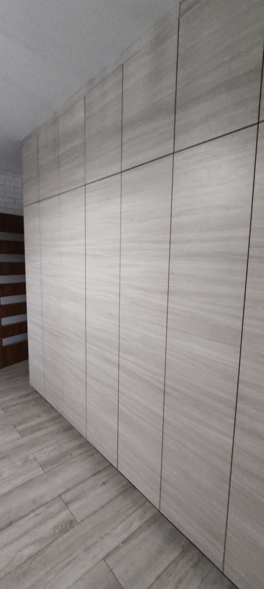 Długa szafa wnękowa z panelami o fakturze drewna, dopasowana kolorystycznie do podłogi, widoczna z perspektywy podłogi, z fragmentem drzwi w tle.