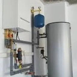 Nowoczesna instalacja grzewcza z zbiornikiem akumulacyjnym i osprzętem, widoczna w surowym wnętrzu z betonowym sufitem.