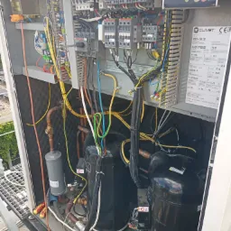 Wnętrze obudowy agregatu chłodniczego Clivet WSAT-XEE 262 z widocznymi kompresorami, orurowaniem miedzianym, filtrem-odwadniaczem, elementami elektrycznymi i sterowaniem, na dachu budynku.