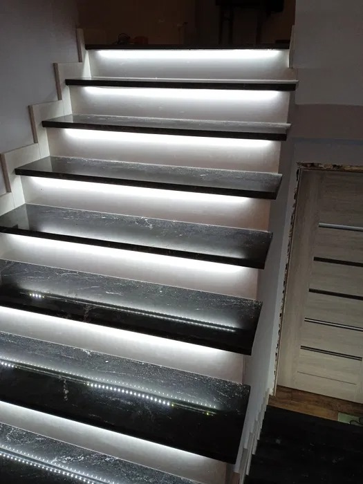 Schody z czarnego kamienia z podświetleniem LED zamontowanym pod każdym stopniem, widoczne z boku.