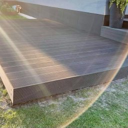 B&B Gw Sp Zoo - Nowoczesny taras z kompozytowych desek w odcieniach szarości, z subtelnym oświetleniem słonecznym, donice z kwiatami na schodach wejściowych.