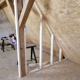 B&B Gw Sp Zoo - Wewnętrzna ściana szkieletowa w trakcie budowy, widoczne drewniane słupki i metalowe łączniki, w tle płyta OSB i stół roboczy z narzędziami.