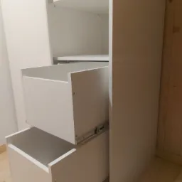 Biała szafa z dwoma wysuniętymi szufladami, widoczne prowadnice, proste wykończenie.