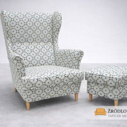 Zakład Usługowy Tapicerstwo Meblowe Jacek Sęków - Wysoki fotel uszak i pufa w geometryczny wzór, tapicerowane tkaniną w odcieniach bieli i błękitu, na tle jasnoszarego studia. Widoczne drewniane nóżki.