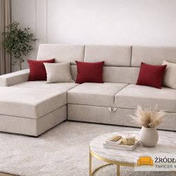Zakład Usługowy Tapicerstwo Meblowe Jacek Sęków - Beżowy narożnik z funkcją spania, z bordowymi i kremowymi poduszkami, na tle jasnego wnętrza. Na pierwszym planie stolik z dekoracjami.