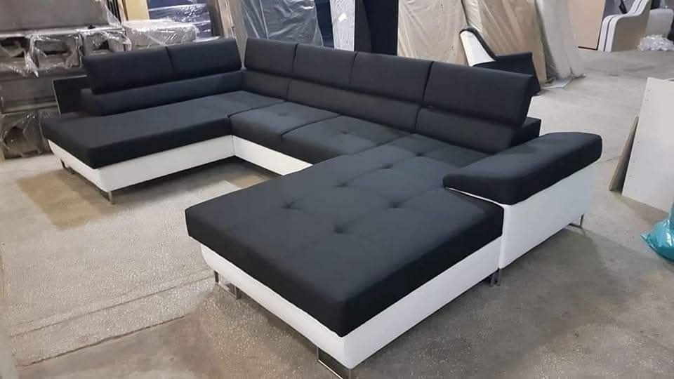 Nowoczesny narożnik tapicerowany w kolorze czarnym z białymi bokami i metalowymi nóżkami, widoczny w przestrzeni produkcyjnej.