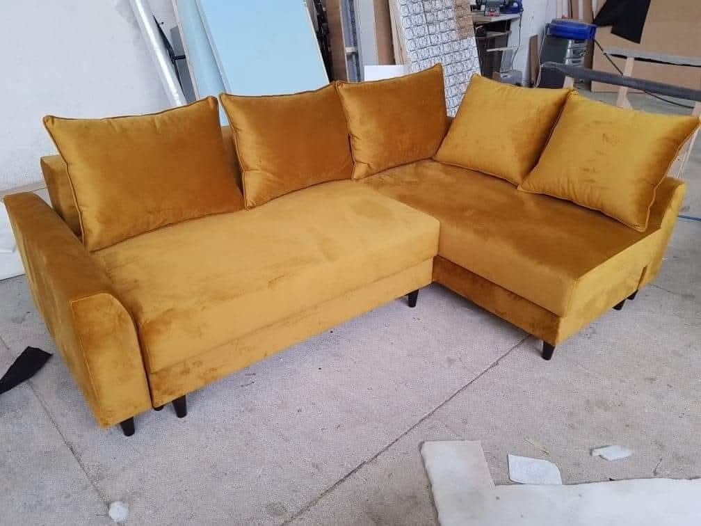 Złoty, welurowy narożnik z poduszkami, na niskich, czarnych nóżkach. Widoczne detale tapicerki i szwy. Ujęcie z bliska, prezentujące fakturę materiału.