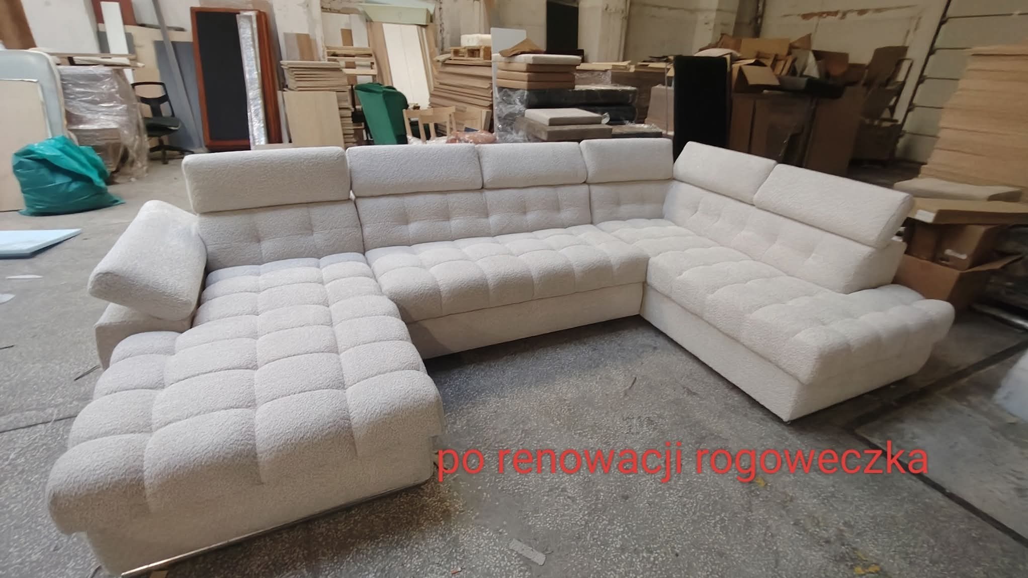 Jasna, narożna sofa z pikowanym wzorem w warsztacie. Widoczne materiały i narzędzia tapicerskie w tle. Ujęcie z niskiego kąta podkreśla rozmiar mebla.