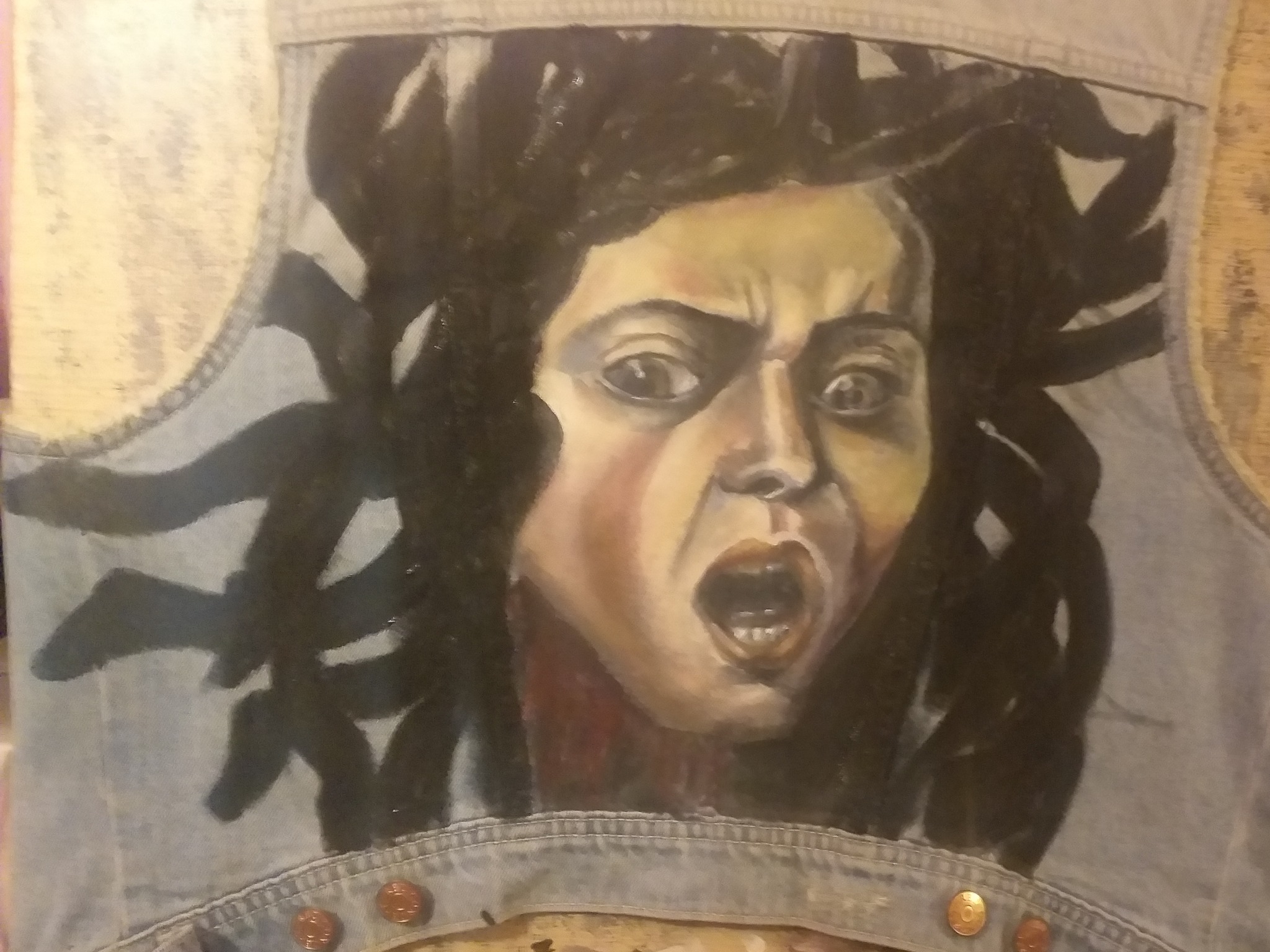 Portret krzyczącej osoby namalowany farbami na jeansowej kamizelce, widoczne niedoskonałości malunku i faktura materiału.