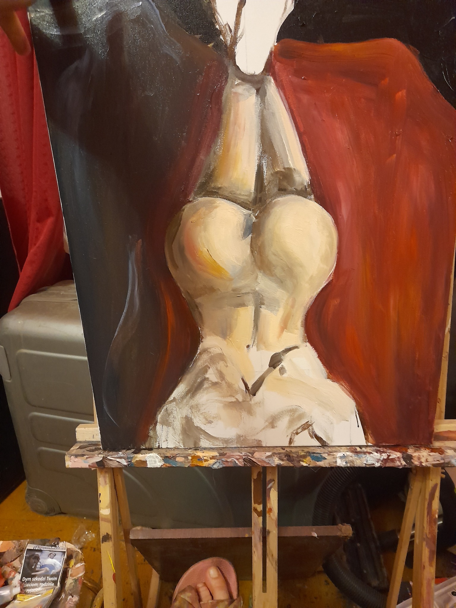 Niedokończony obraz olejny przedstawiający akt kobiecy na sztaludze, widoczny fragment stopy malarza i paczka papierosów na dolnej półce sztalugi.