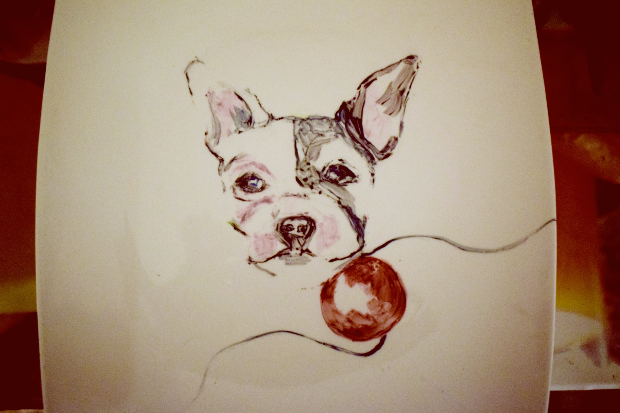 Ręcznie malowany portret psa rasy Boston Terrier z czerwoną kulką na ceramicznym talerzu.