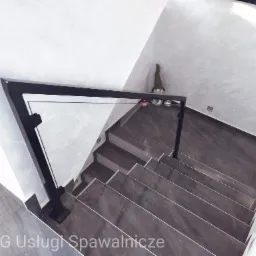 Nowoczesne schody z ciemnymi płytkami i szklaną balustradą z czarnymi metalowymi elementami, widok z góry, dekoracyjny skrzat na ścianie.