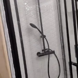 Nowoczesna kabina prysznicowa z czarną armaturą na tle białych, wzorzystych płytek.