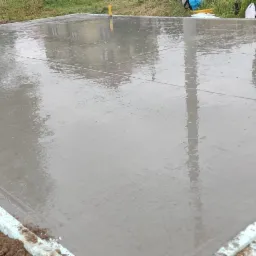 Świeżo wylany, mokry beton na przygotowanym podłożu z izolacją obwodową. Widoczne odbicia budynków w gładkiej powierzchni betonu.