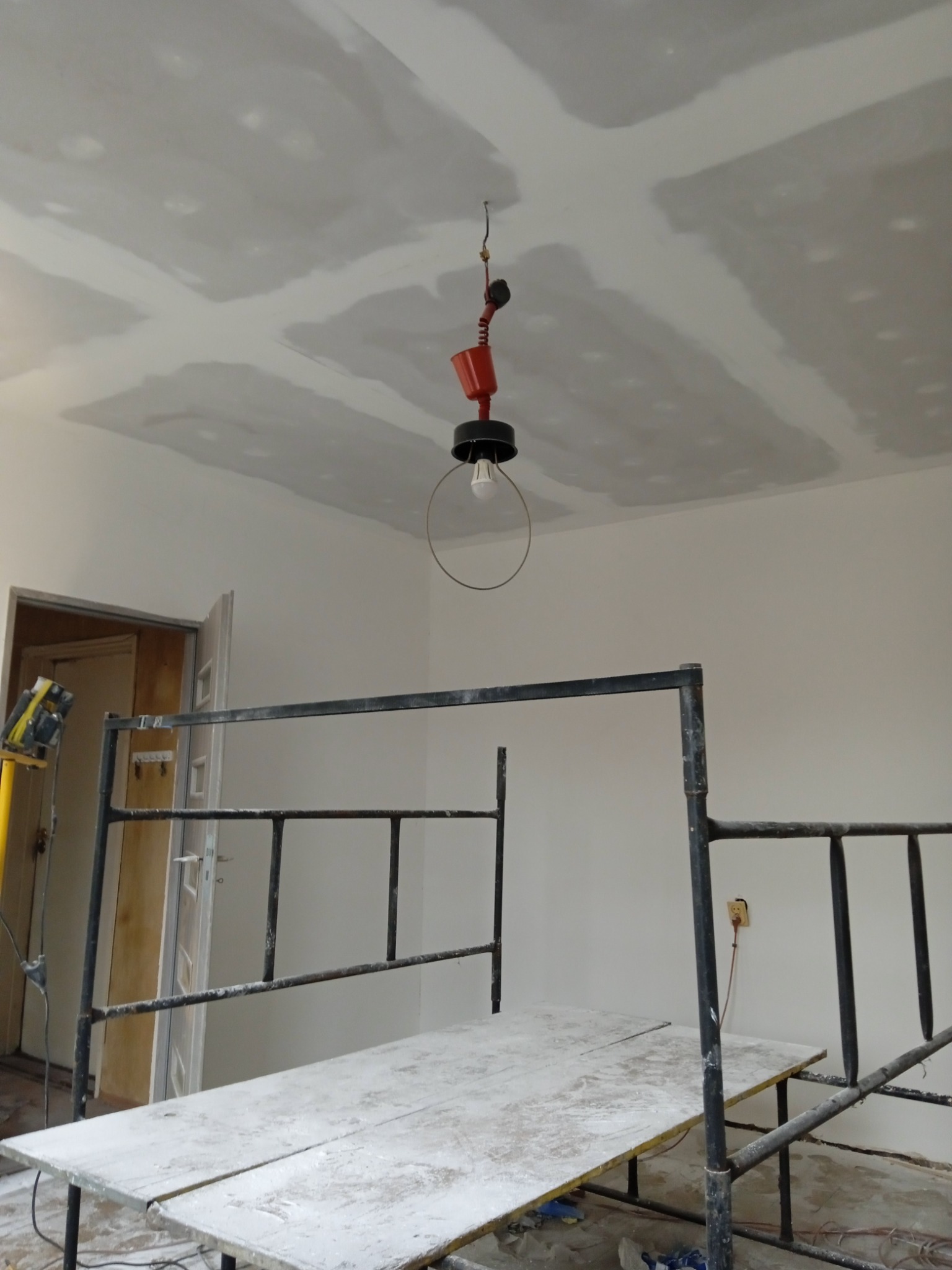Sufit z płyt gipsowo-kartonowych po szpachlowaniu, widoczne łączenia, oświetlenie robocze i rusztowanie w pomieszczeniu w trakcie remontu.