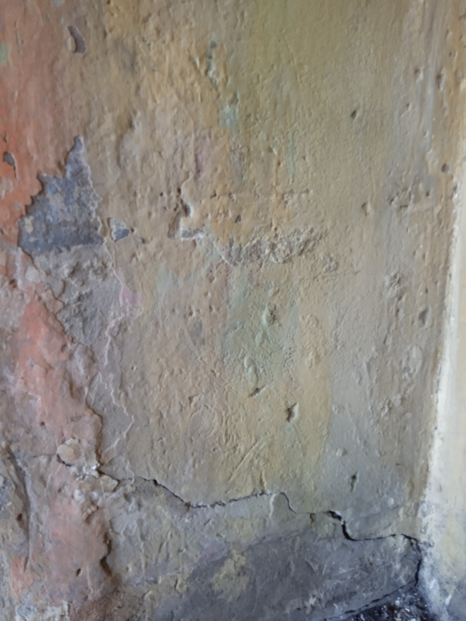 Nierówna, popękana ściana z widocznymi warstwami starej farby i szpachli w odcieniach beżu, szarości i pomarańczu, ukazująca stan przed renowacją.