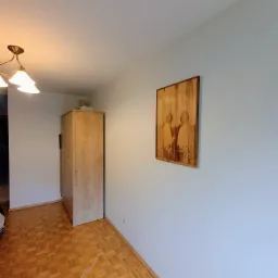 Jasne wnętrze pokoju z parkietem, szafą i obrazem na ścianie pomalowanej na jasny odcień niebieskiego.