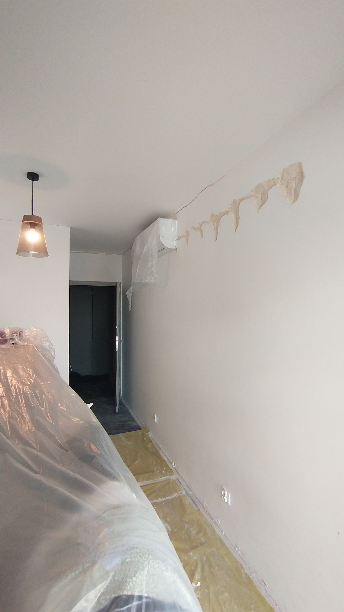 Przygotowania do malowania: zabezpieczona folią podłoga i meble, klimatyzator owinięty folią, ślady po naprawie ubytków na ścianie