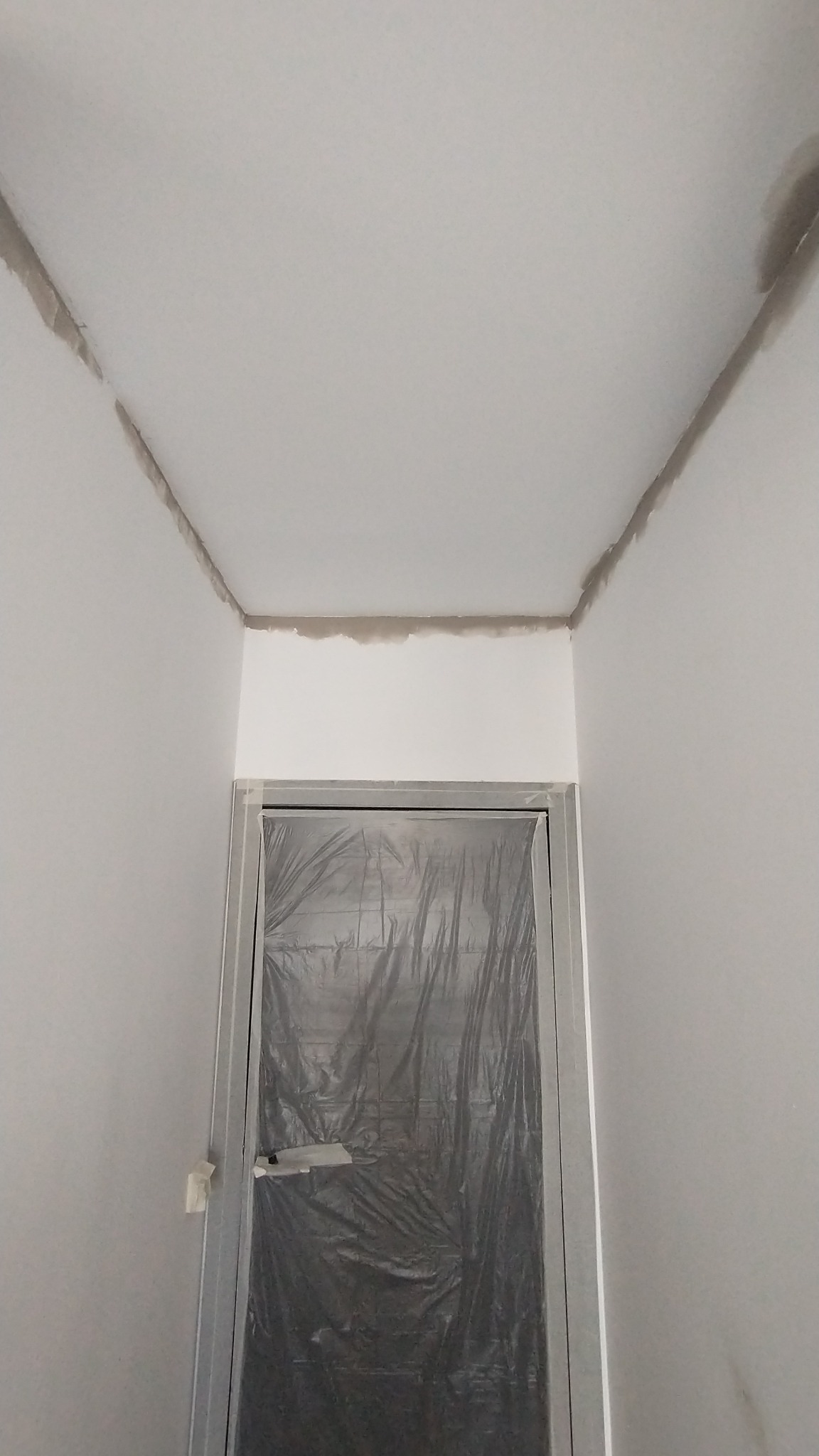 Świeżo pomalowane wnętrze z widocznymi śladami szpachlowania przy suficie i zabezpieczonymi folią drzwiami.