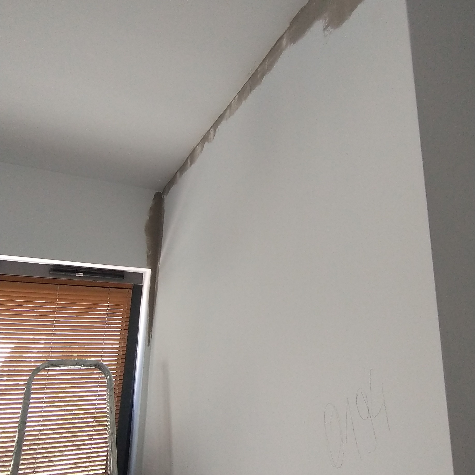 Przygotowanie ściany do malowania: szpachlowanie łączenia ściany i sufitu, widoczna drabina i okno z żaluzjami.