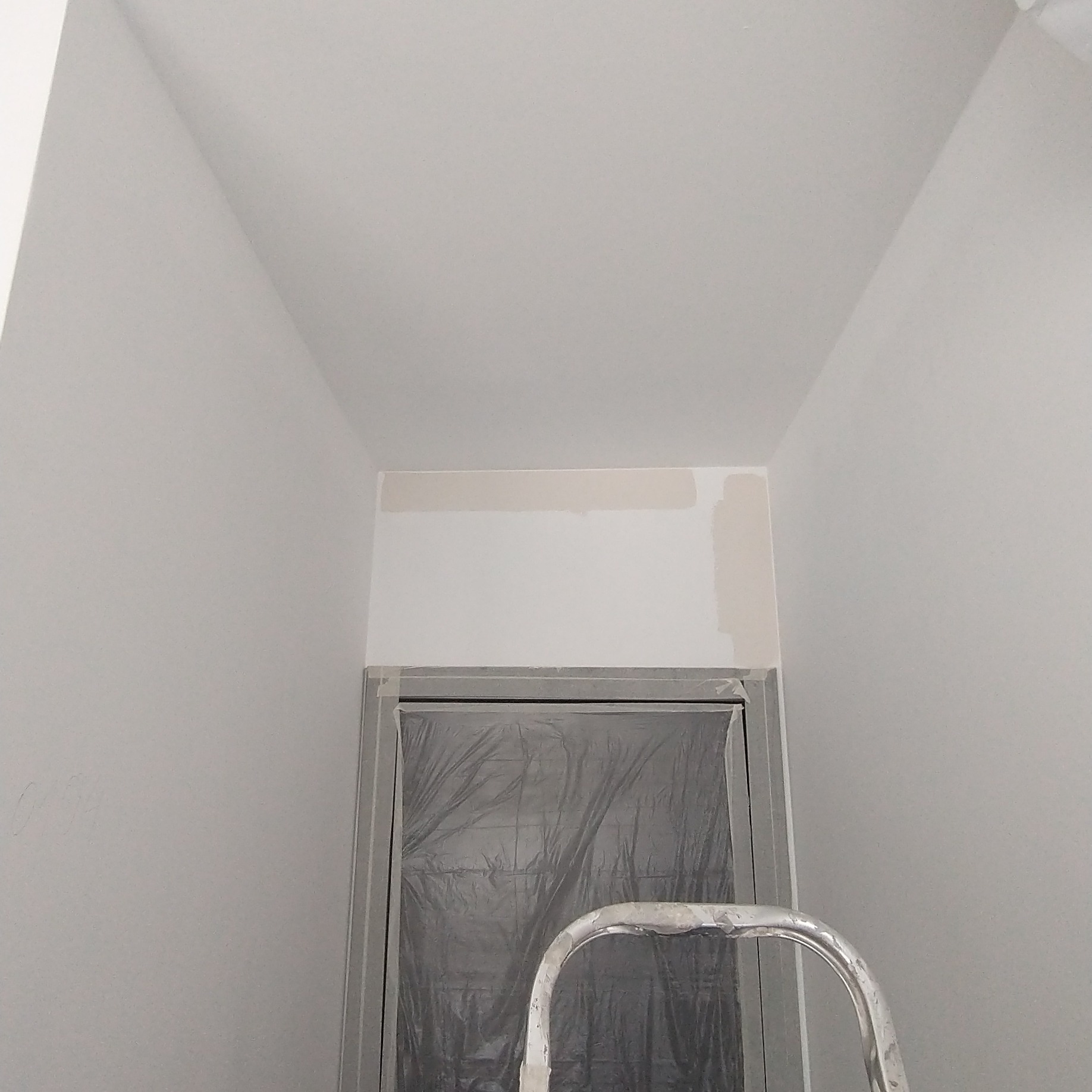 Wnętrze w trakcie malowania: fragment ściany z próbkami koloru nad zabezpieczonym folią otworem drzwiowym, widoczny fragment drabiny.