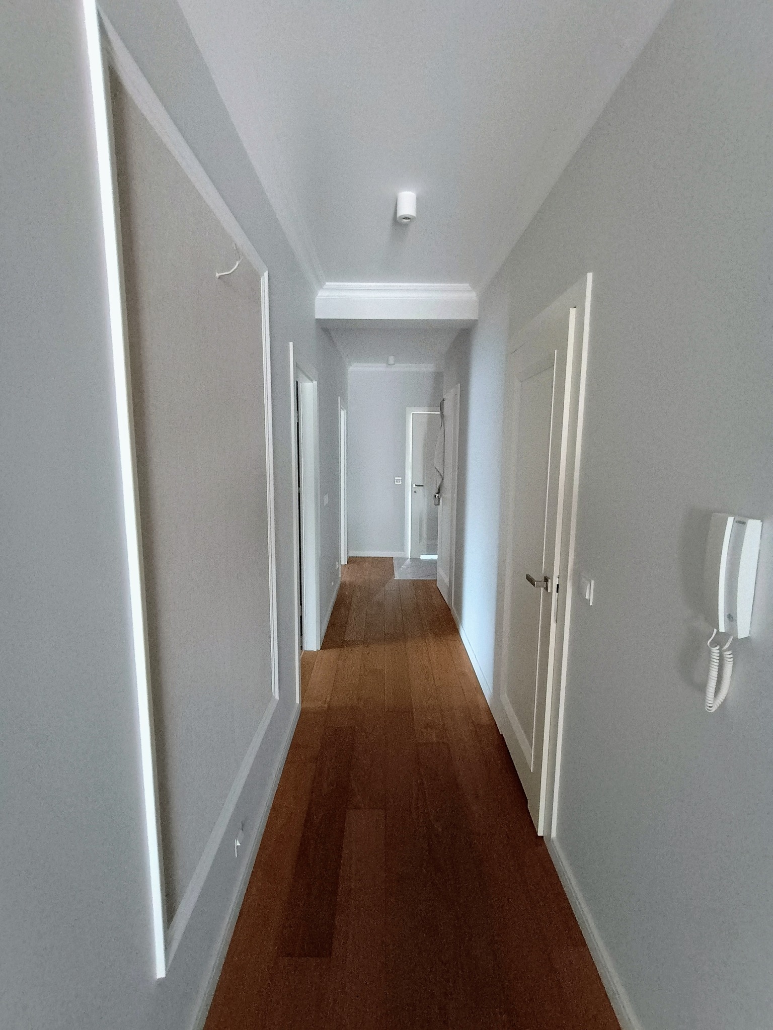 Wnętrze korytarza w odcieniach szarości z drewnianą podłogą, białymi drzwiami i dekoracyjnymi listwami ściennymi.