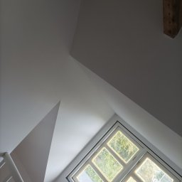 Usługi remontowe - Poddasze z oknem w białej ramie, fragment schodów i drewniane belki stropowe