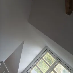 Poddasze z oknem w białej ramie, fragment schodów i drewniane belki stropowe