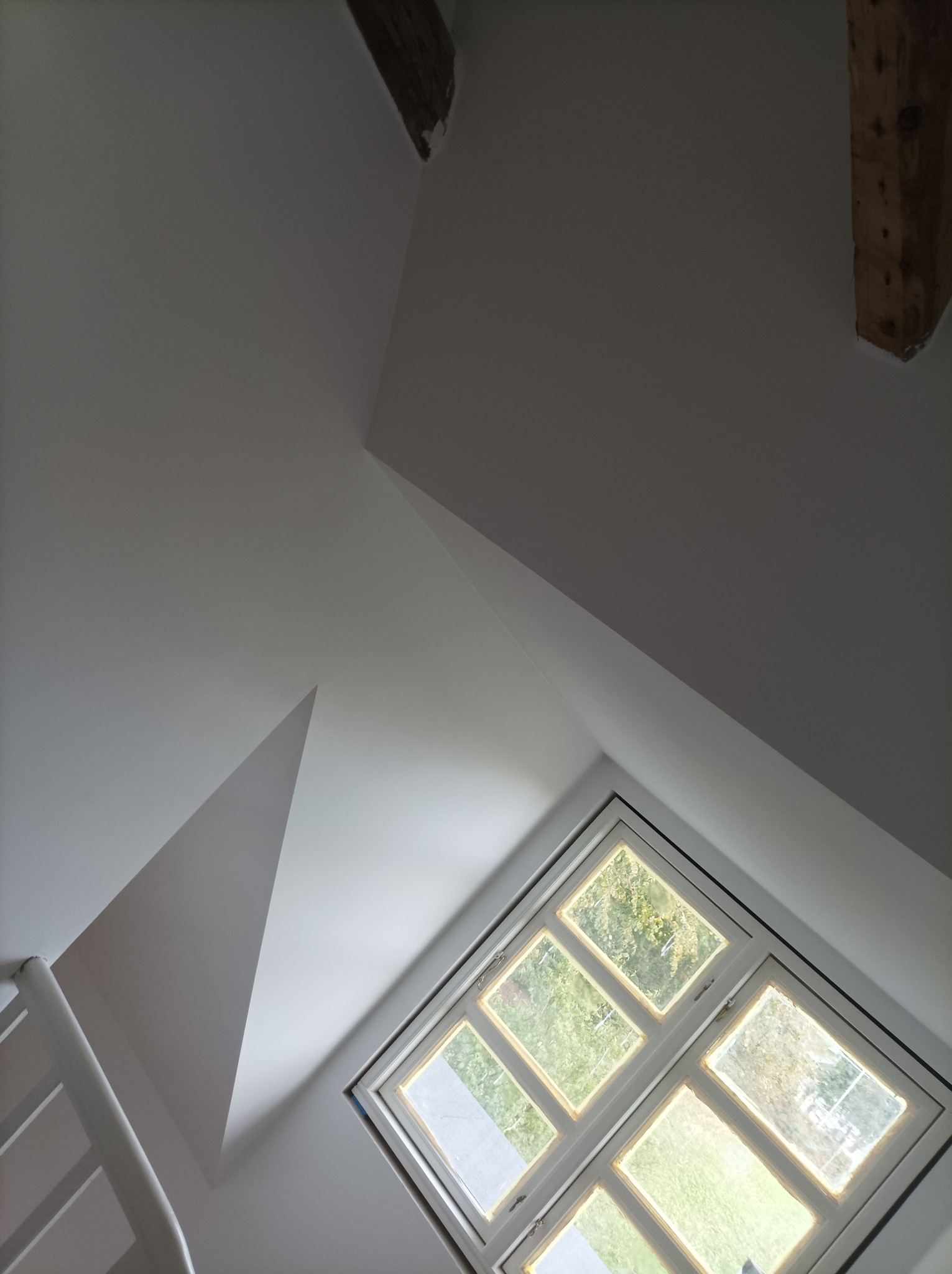 Poddasze z oknem w białej ramie, fragment schodów i drewniane belki stropowe