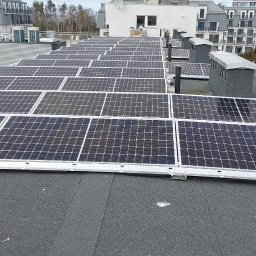 OWN Energy - Rząd paneli fotowoltaicznych na płaskim dachu budynku mieszkalnego, widok z góry, szare niebo w tle.